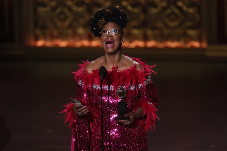 A person in formal wear looks up while making a speech and holding an award.