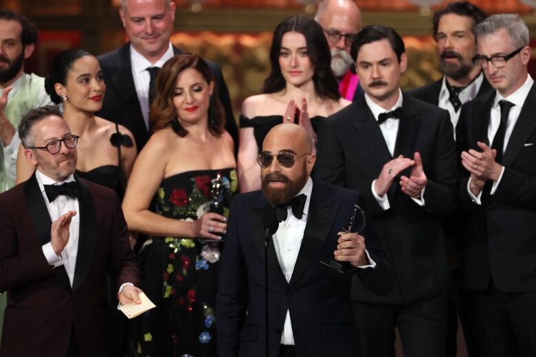  A group of men and women gather on a stage holding award statues.