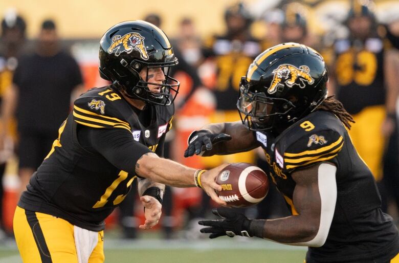 Hamilton Tiger Cats quarterback Bo Levi Mitchell (19) hands off to Hamilton Tiger Cats running back James Butler (9) during first half CFL football action against the Saskatchewan Roughriders, in Hamilton on Sunday, June 16, 2024. 