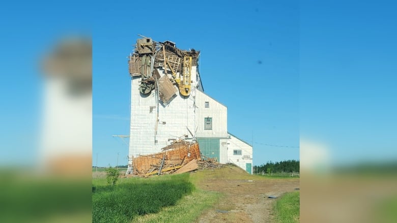 A grain elevator on the prairie against a blue sky. The top of the structure is broken and collapsed.