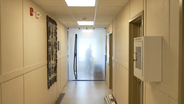 A hallway with a closed-off section at the end, where a worker's silhouette can be seen using a machine.