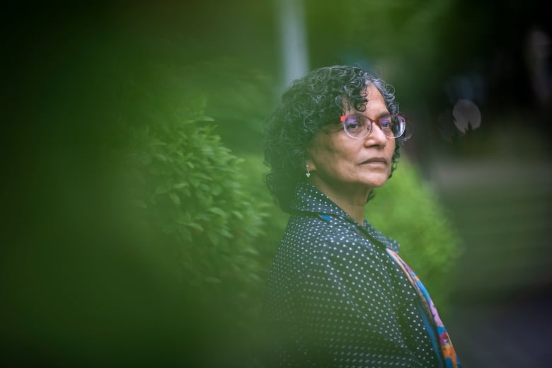 A South Asian woman is pictured while standing against a hedge.