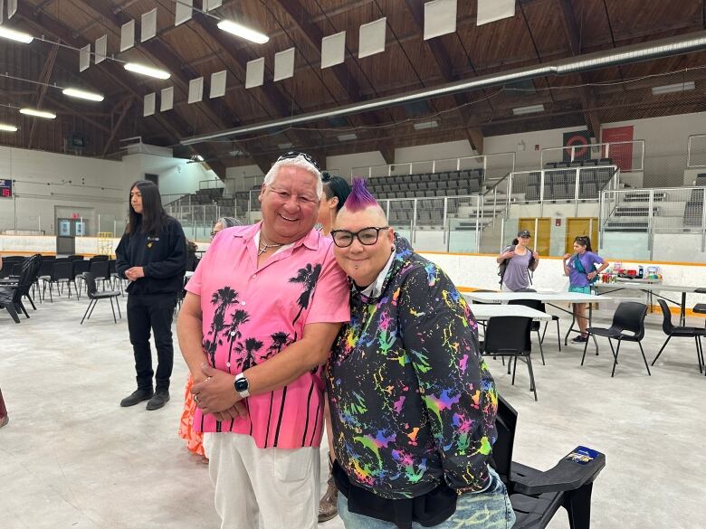 Two people stand together and smile in an arena.