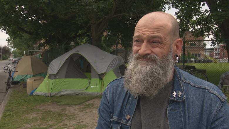 A man with a long beard standing in front of an encampment. 