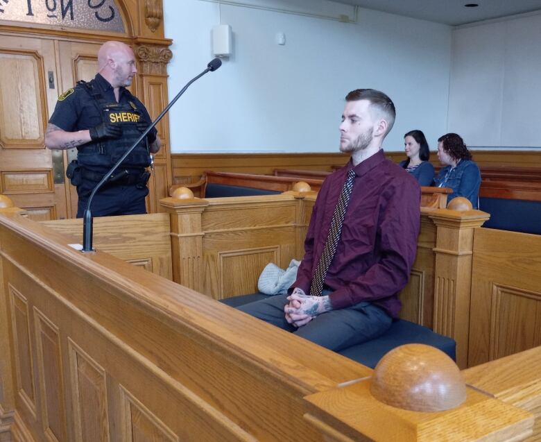 Man in burgundy dress shirt sitting in court room.