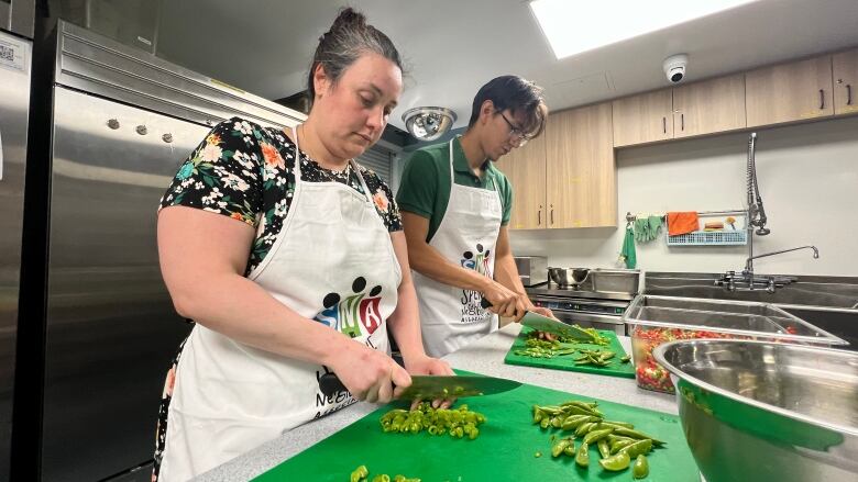 A woman and a man are standing in a kitchen chopping vegetables.