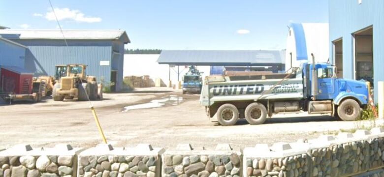 A truck with the words 'United Concrete & Gravel' along its side is seen in an industrial parking lot, with more vehicles and blue buildings behind it.