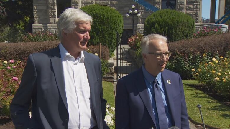 Two white men with grey hair stand outside. 