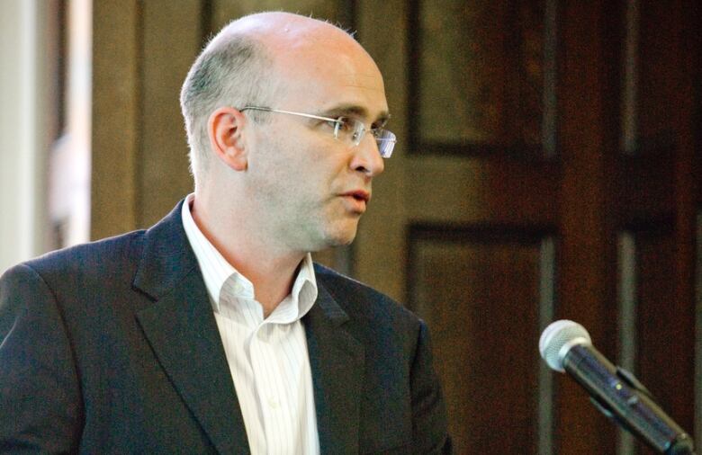 a man in a dark suit speaks at a microphone 