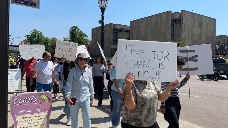 People holding signs walk on a sunny street across from the Confederation Centre in downtown Charlottetown.