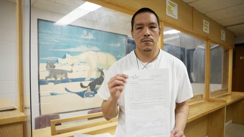 A man wearing a white shirt in a prison visitation room holds a piece of paper. 