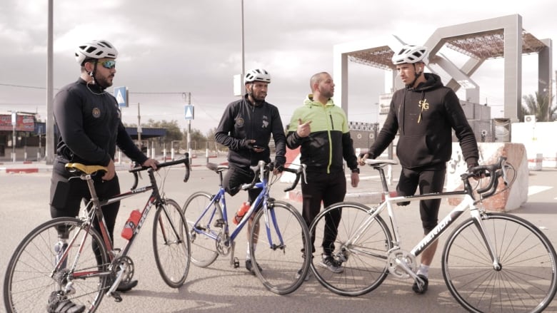 Three Para cyclists stand with their bikes while taking direction from a coach.