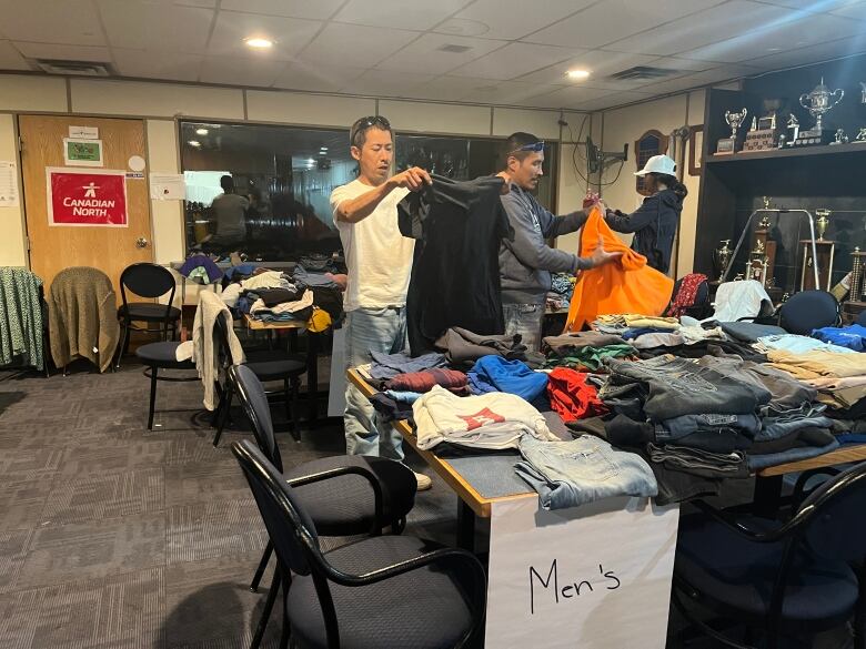 Three people look through tables of clothing 