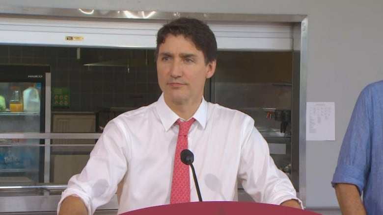 A man wearing a red tie speaks at a podium.