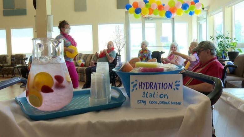 People sit in chairs behind a table with a pitcher of water, cups, and a sign saying Hydration Station.