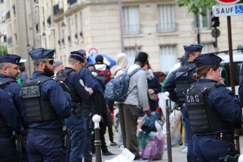 Police officers in blue uniforms stand in a group as they evict a group of people living in an encampment.