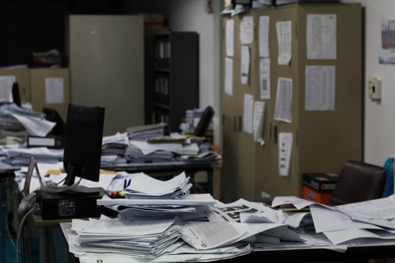 A cluttered desk in an office space. There are documents everywhere.