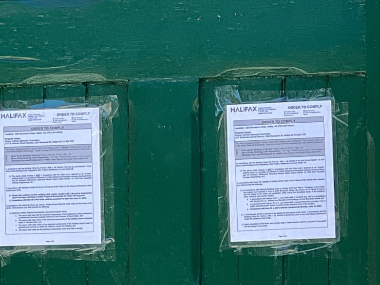 Two orders to comply notices are seen on a green door.