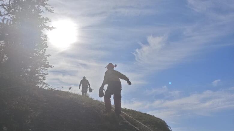 Two firefighters are seen from behind walking up a hill.