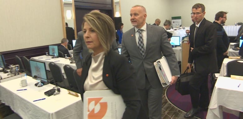 A woman with a bindert in hard walks out of a meeting room.