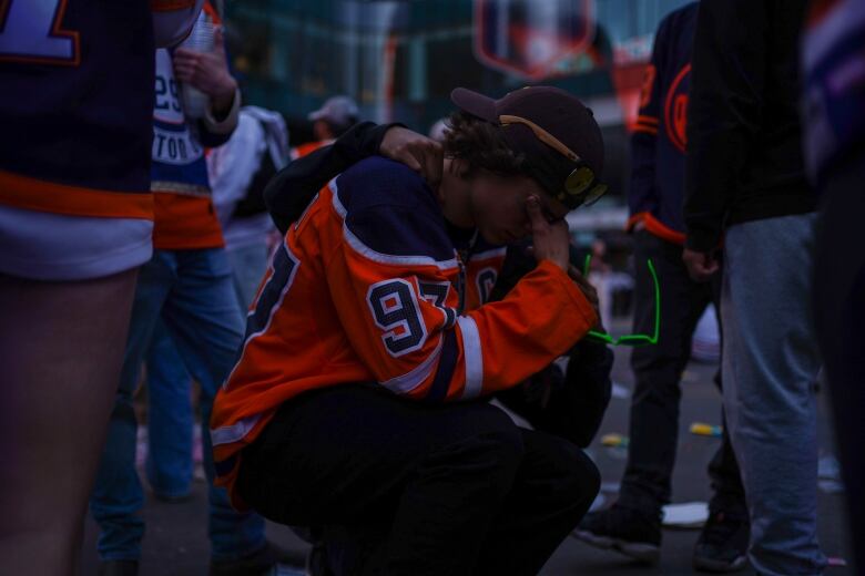 A man in an Oilers jersey crouches down amidst a crowd.