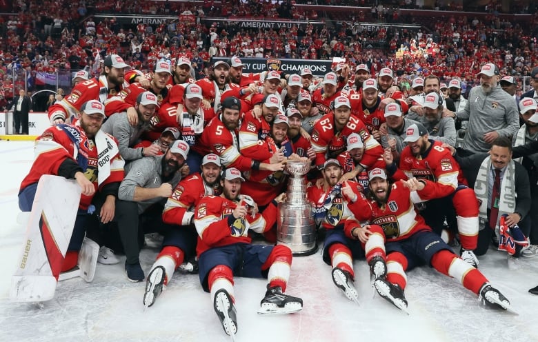 A male ice hockey team poses for a group picture on the ice around the Stanley Cup.