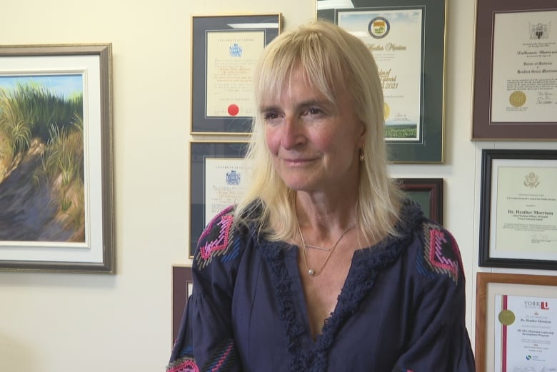 Heather Morrison sitting in her office with framed diplomas and degrees on the wall behind her.