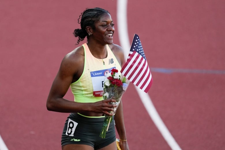 An athlete smiles holding a U.S. flag and flowers