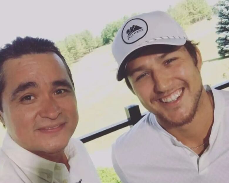 Two people pose for a selfie with a golf course behind them