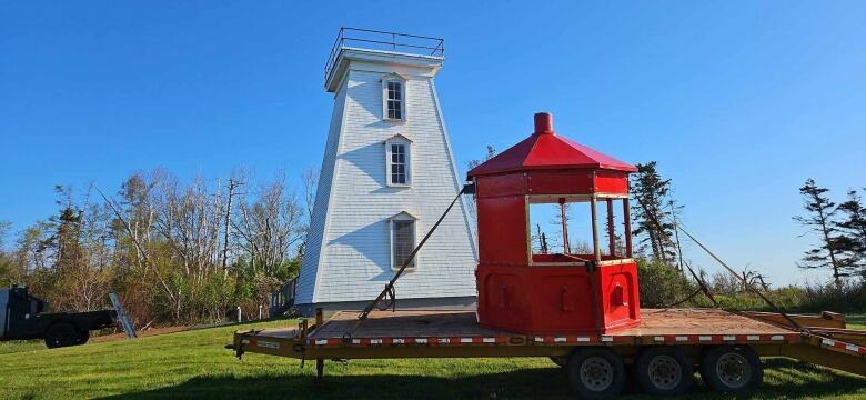 The lanten of a lighthouse is on the ground in front of the lighthouse. 