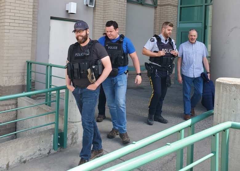 Two RCMP officers in tactical vests, a uniformed RCMP member, and a man in a blue shirt leave the Prince George courthouse. 