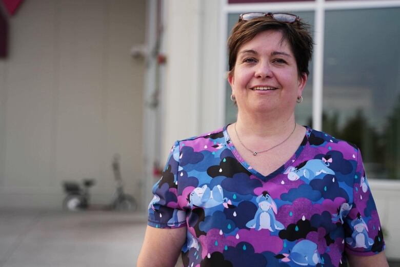 A smiling woman wearing a purple and blue Winnie the Pooh shirt stands in front of a community centre.