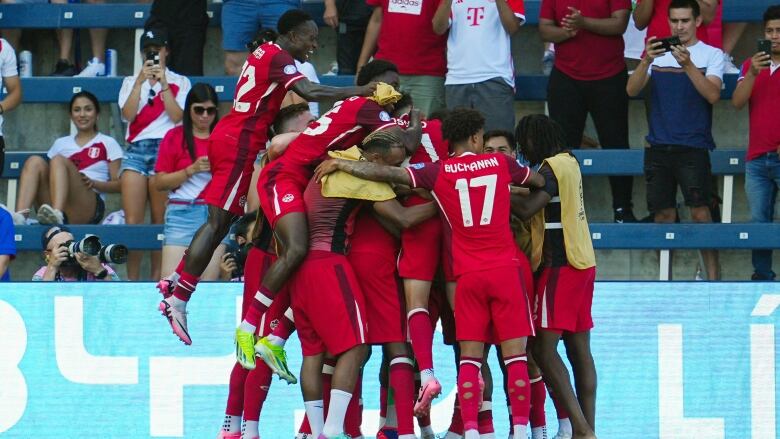 Members of a men's soccer team wrap their arms around each other in celebration on the field.