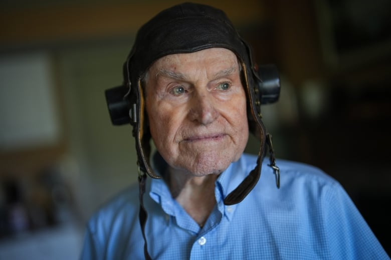 An older white man wearing an air force helmet looks to his side. 