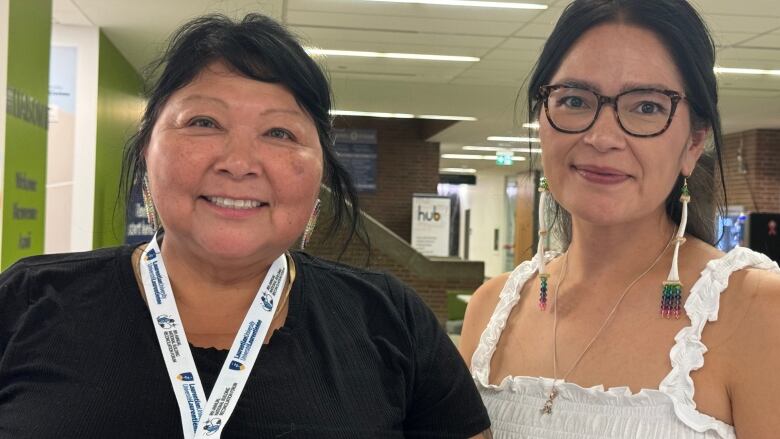 Two women stand smiling at the camera beside each other