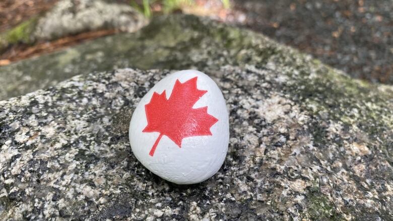 A stone painted white with a red maple leaf on it.