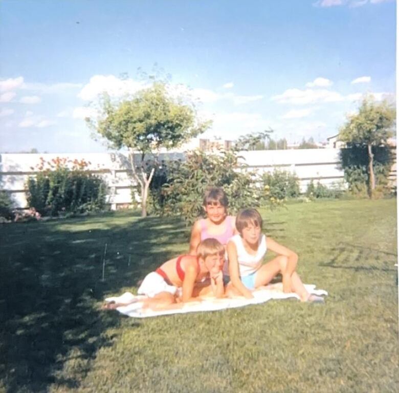 An old photograph shows three young girls sitting in a backyard on a sunny day.