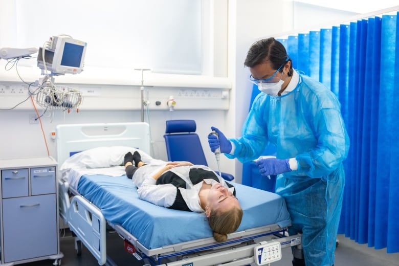 A scientist prepares to administer a low dose of SARS-CoV-2 to the nose of a human volunteer lying down. 