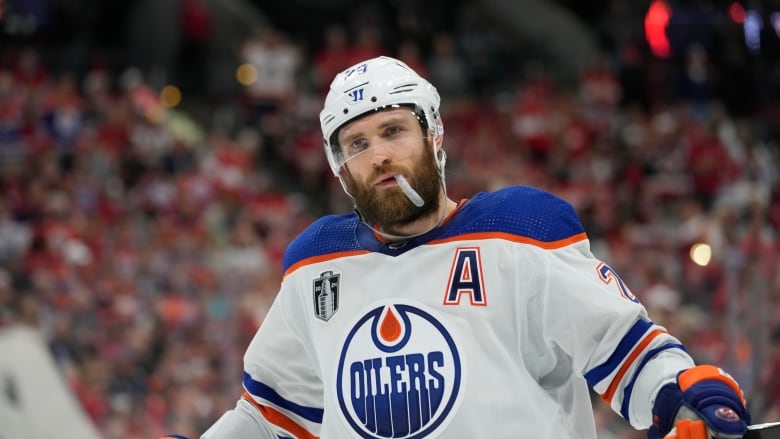 A man stands in an ice arena wearing a hockey helmet and holding a stick. 