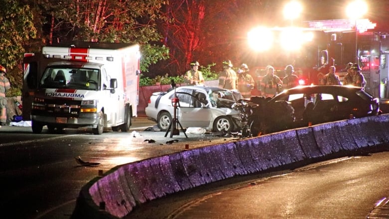 An ambulance beside two badly damaged cars on a highway.