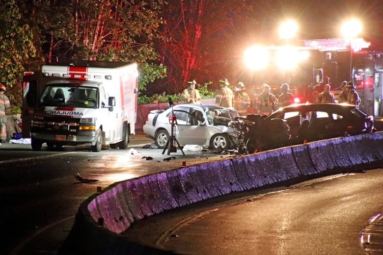 An ambulance beside two badly damaged cars on a highway.