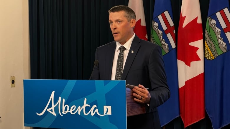 A man in a suit stands behind a lectern. 