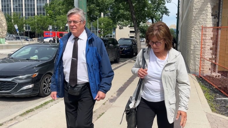 A man wearing a blue coat and shirt and tie is picturing walking with a woman on a sidewalk.