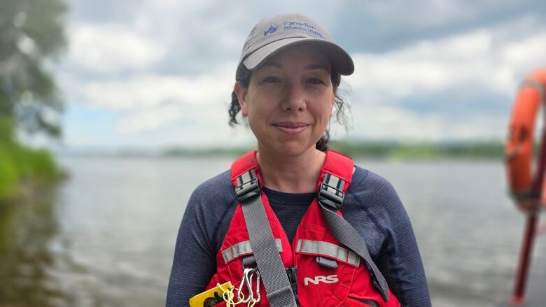 A dark-haired woman in a ball cap and a life jacket. 