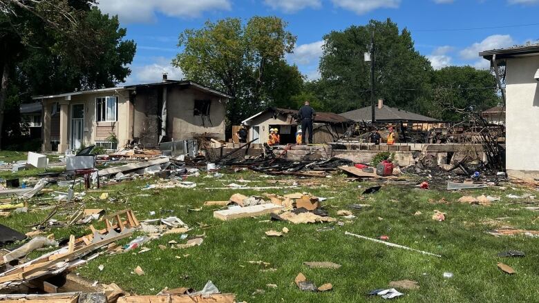 A residential street with several damaged houses, lots of debris and a space where a house once stood.