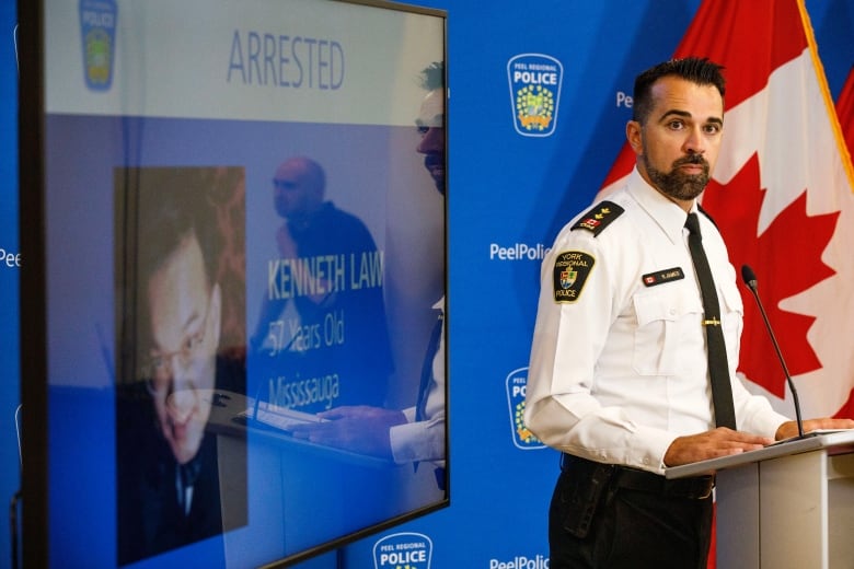 A police officer in a white shirt near a blue screen displaying a picture of Kenneth Law