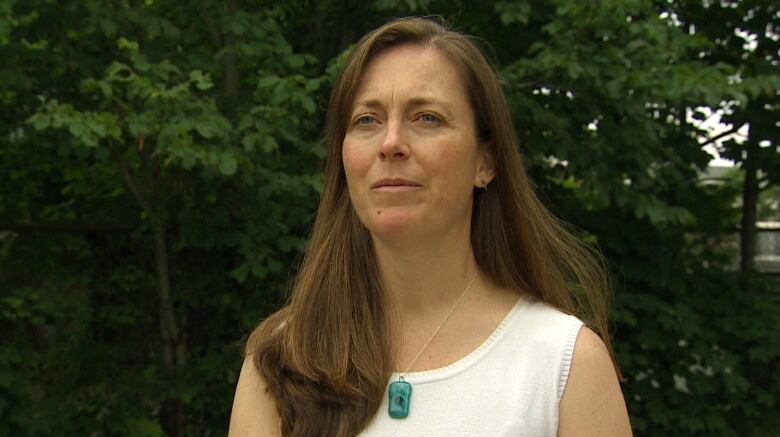 A woman stands in front of trees.