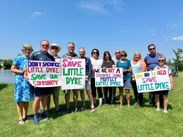 A group of people stand holding signs of protest against a rock quarry.