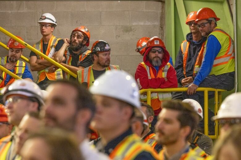 People in safety vests and helmets gathered near yellow railing.