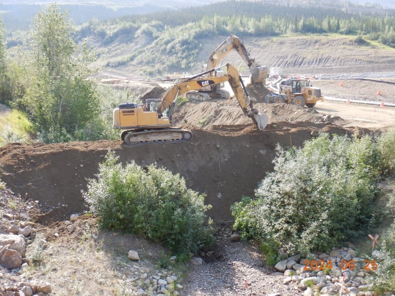 Heavy machinery builds an earthen dam.